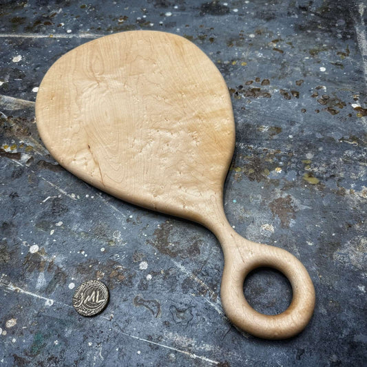 birdseye maple serving board with round handle on workshop surface