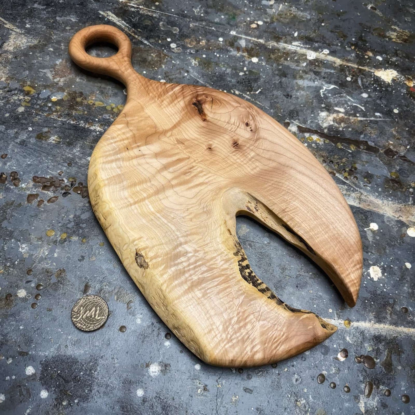 curly maple serving board with lobster claw shape and round handle on workshop surface