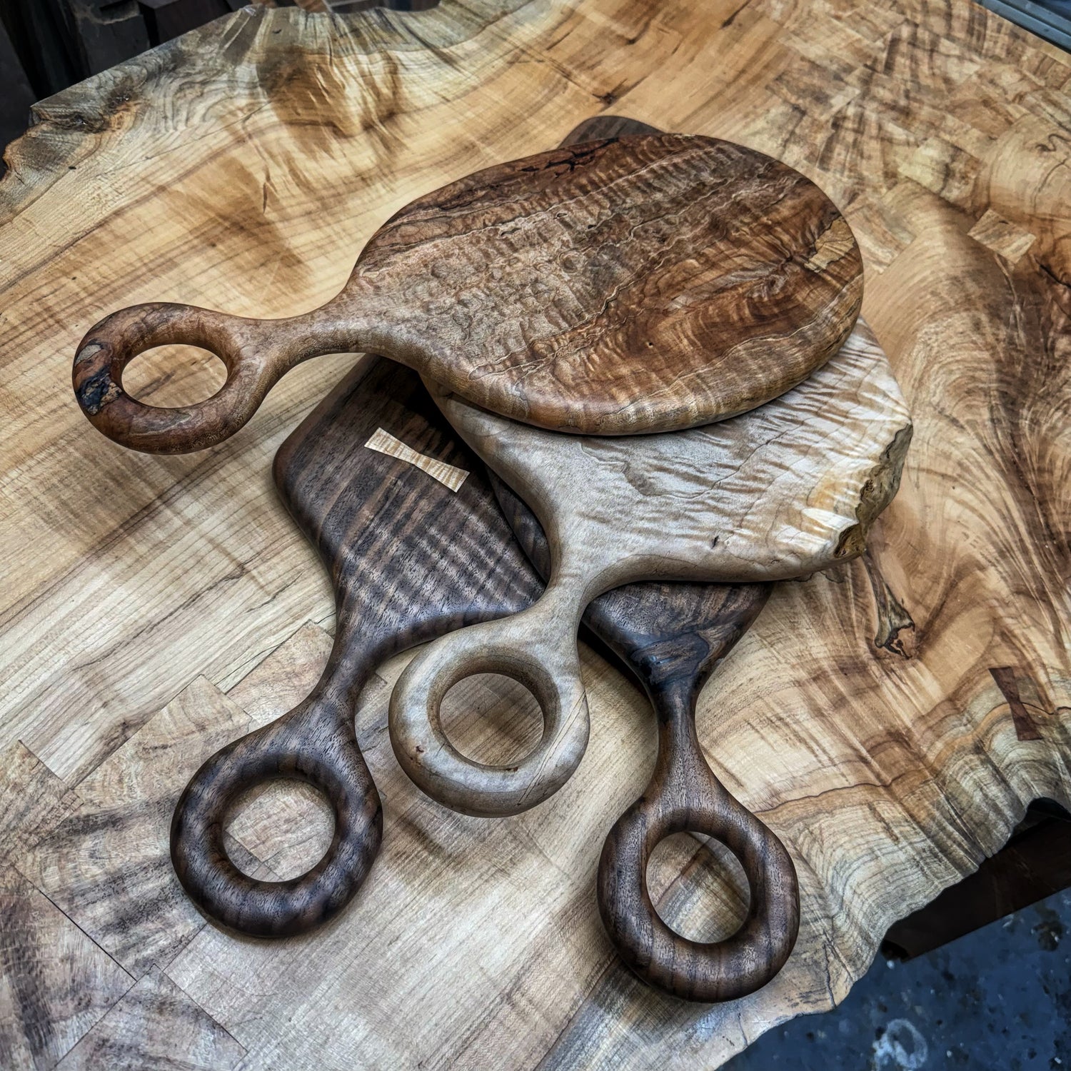 stack of handcrafted serving boards made from figured hardwoods with round sculpted handles on a live edge slab