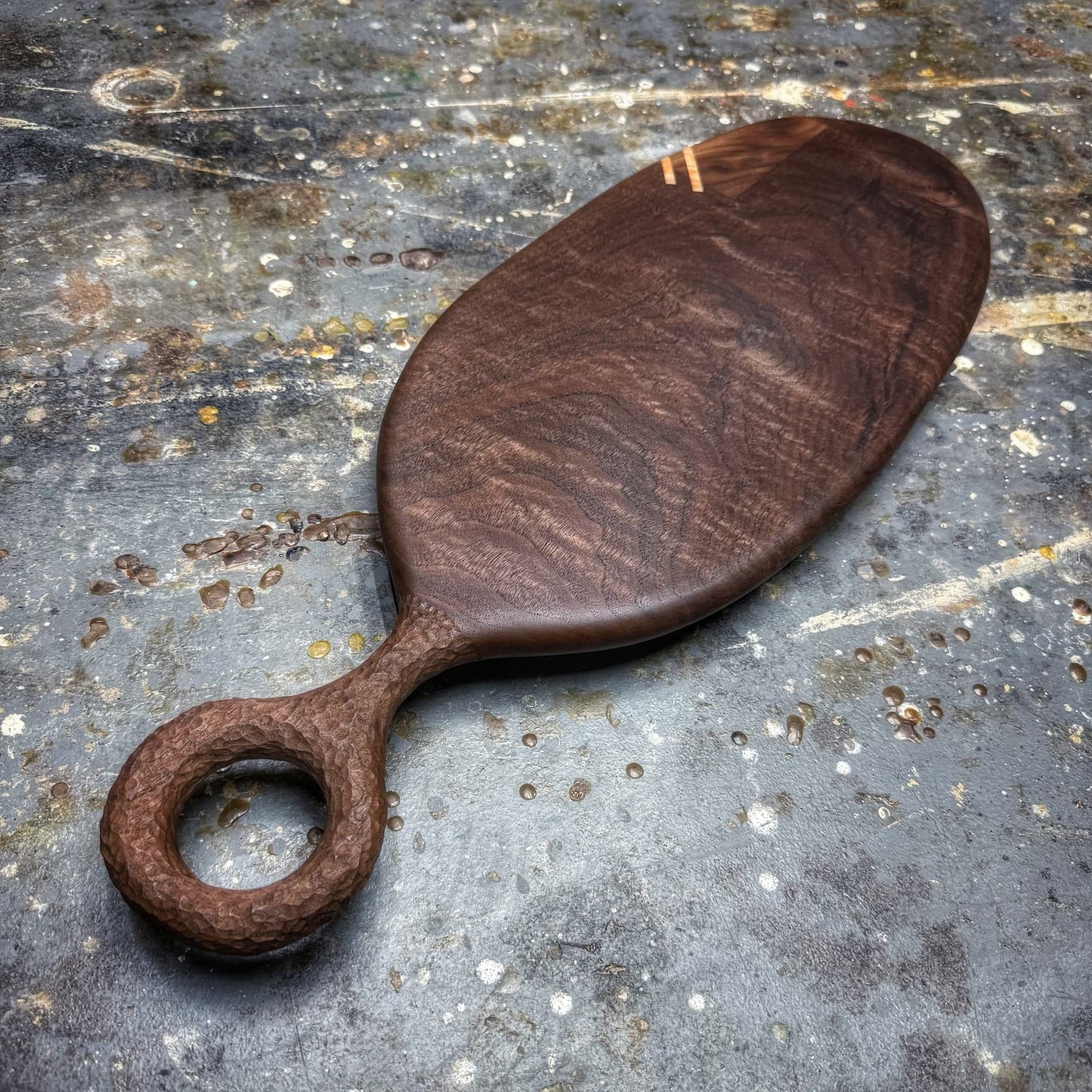 A dark brown wooden serving board with a loop handle, photographed on a textured, weathered gray stone surface.