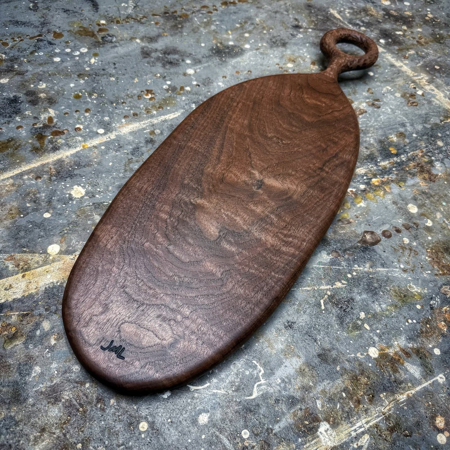 A dark brown wooden serving board with a loop handle, displayed on a textured, weathered gray stone surface.
