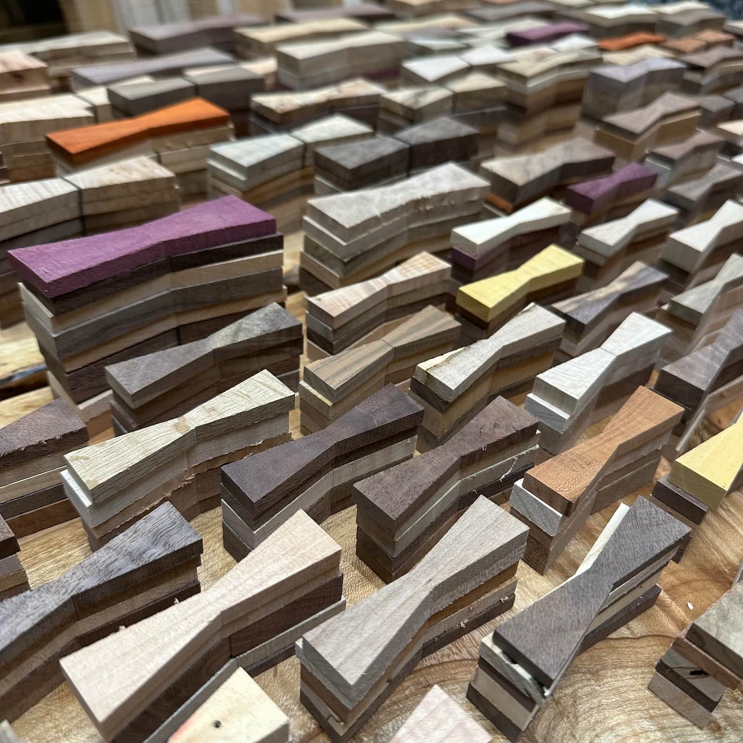 Pile of handcrafted hardwood bow tie inlays in assorted sizes and figured grain