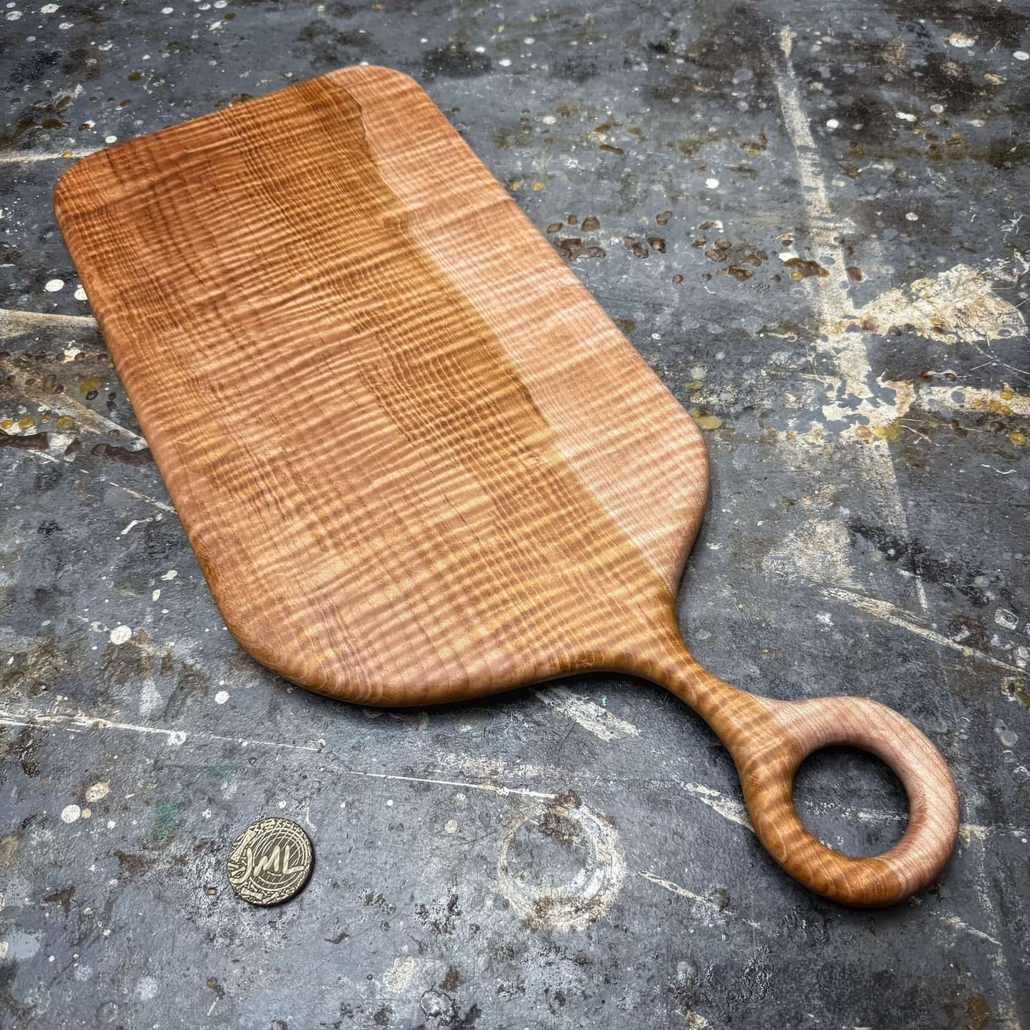 two tone curly maple serving board with round handle on workshop surface