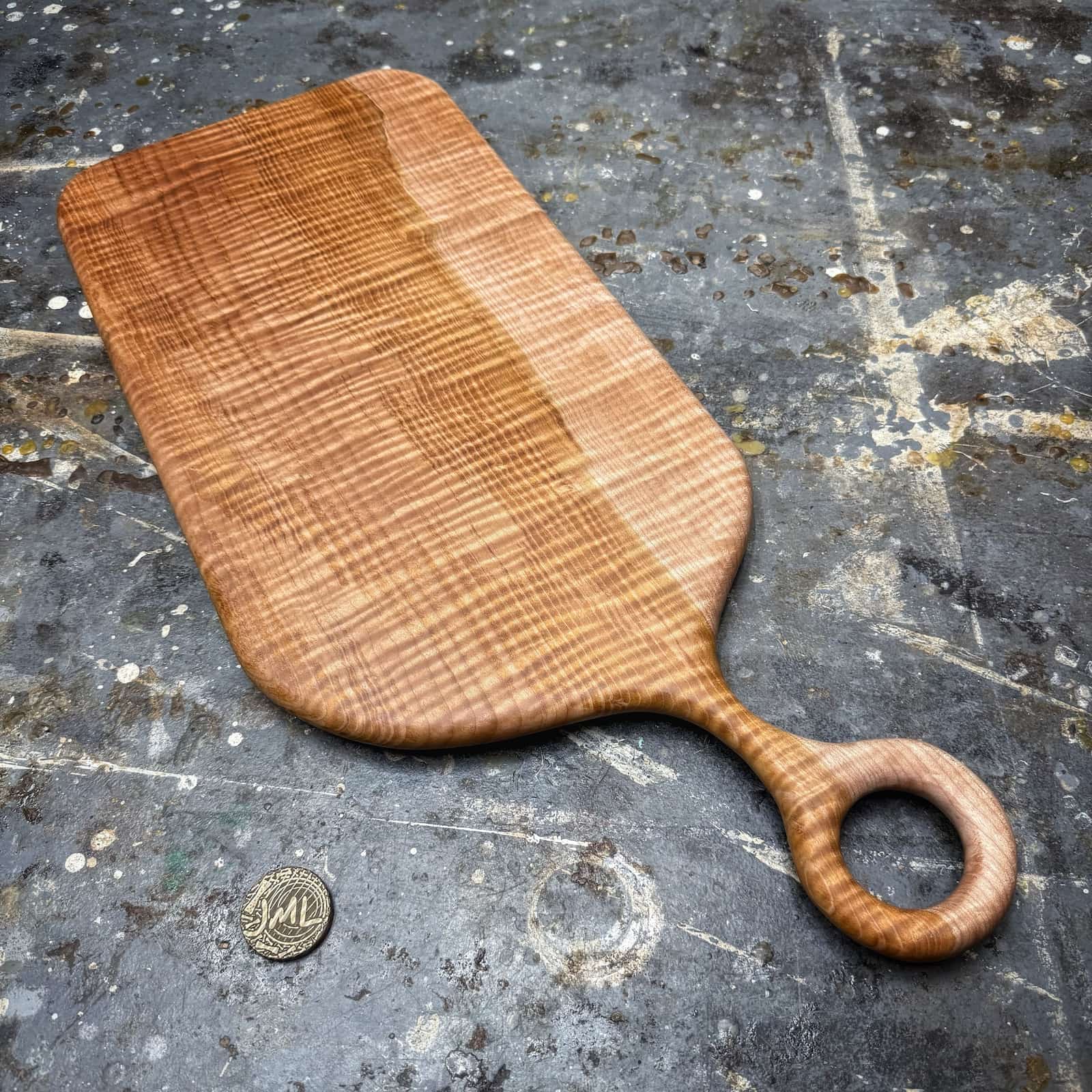 two tone curly maple serving board with round handle on workshop surface